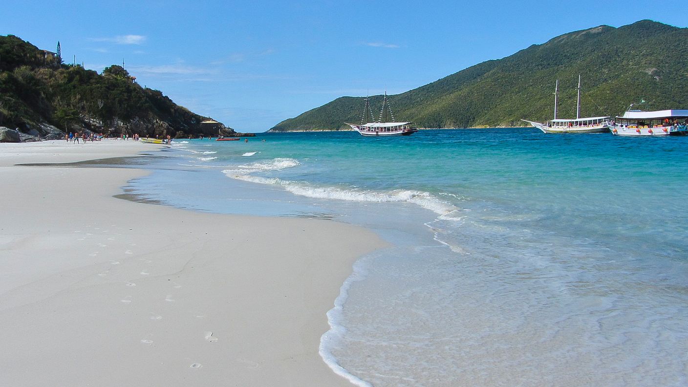 Praia de areia branca com mar azul-turquesa cristalino e veleiros em Arraial do Cabo, Rio de Janeiro