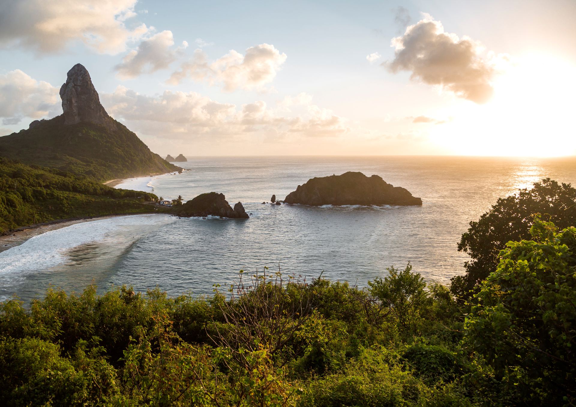 Vista aérea do Morro do Pico ao pôr do sol em Fernando de Noronha, Pernambuco, com mar verde e a baía abaixo