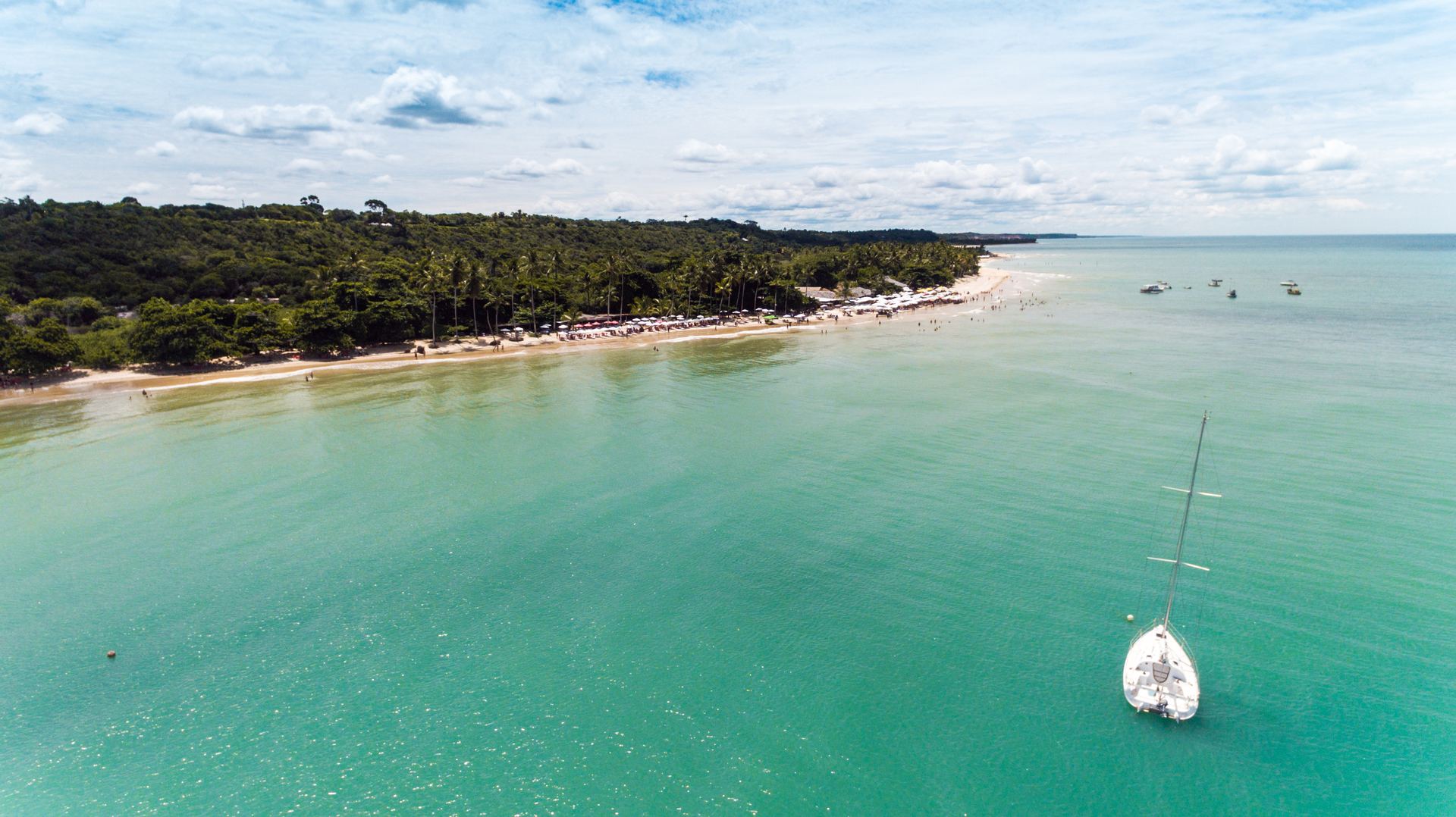 Vista aérea da Praia dos Coqueiros em Trancoso, Porto Seguro, com mar esverdeado e veleiro